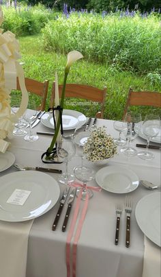 the table is set with white plates, silverware and flowers in glass vases