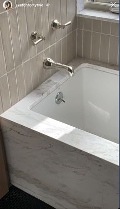 a white bath tub sitting in a bathroom next to a window and tiled flooring