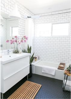 a white tiled bathroom with black and white tile flooring, sink, bathtub and mirror