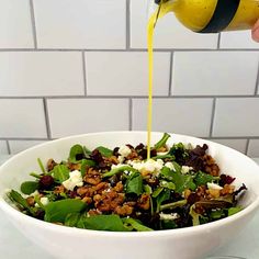 someone pouring dressing into a salad in a white bowl