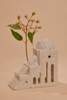 a small white building with a plant growing out of it's side, on a beige background