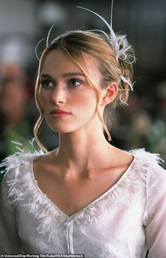 a woman in a white dress with feathers on her head and shoulders, looking off to the side