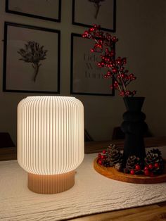 a white lamp sitting on top of a wooden table next to a vase filled with red berries