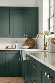 a kitchen with green cabinets and marble counter tops, gold faucets and brass handles