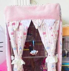 a pink birdcage with curtains and stuffed animals in it