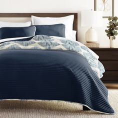 a bed with blue and white comforters in a bedroom next to a night stand