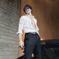 a man in white shirt and black pants standing next to a brick wall