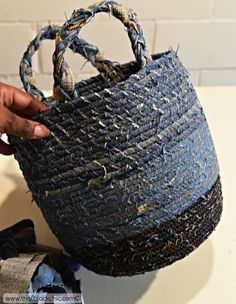 a person holding a woven basket on top of a white table next to a blue cloth bag