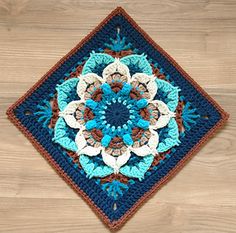 a crocheted square with blue and white flowers on it sitting on a wooden floor