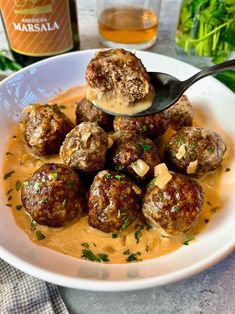 a white bowl filled with meatballs covered in sauce and garnished with parsley