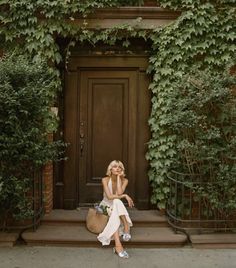 a woman sitting on the steps in front of a door with ivy growing around her