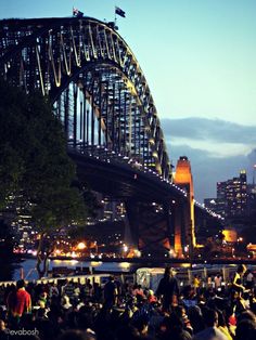 a large group of people standing in front of a bridge at night with lights on