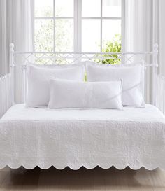 a day bed with white linens and pillows in front of a window, next to a potted plant