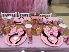 a table set up for a minnie mouse birthday party with pink and gold plates, napkins, cups, utensils and decorations