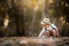 a young boy in a hat crouches down to look at something on the ground