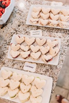 some heart shaped sandwiches are on white plates next to strawberries and raspberries