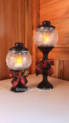 two glass jars with lights in them on top of a white tablecloth covered table