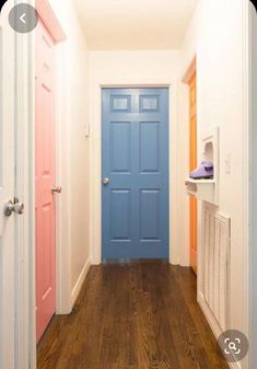 an empty hallway with blue door and wood flooring in front of the doorway to another room