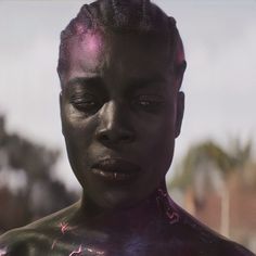 a woman with black paint on her face and chest is looking at the camera while standing outside