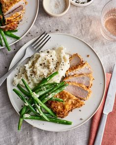 two plates with meat, mashed potatoes and green beans on them next to silverware