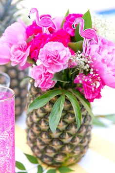 a pineapple vase filled with pink flowers next to a purple glass and some green leaves