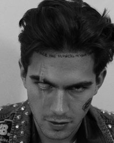 a man with tattoos on his forehead looking down at the camera while wearing a jacket