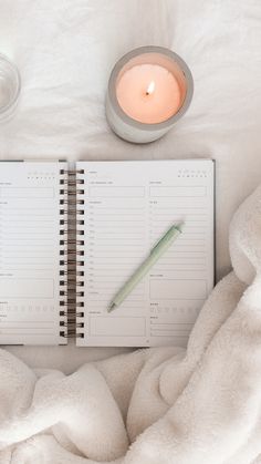 an open notebook with a pen and candle next to it on top of a bed