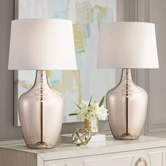 two vases with lamps on top of a dresser