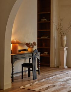 a room with a desk, chair and bookcase in the corner next to a lamp