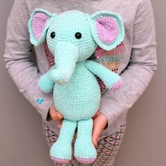 a person holding a small stuffed elephant in their hands and wearing a gray sweater with pink ears