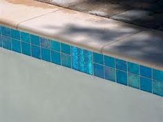 a blue and white tiled swimming pool next to a sidewalk with a tree in the background