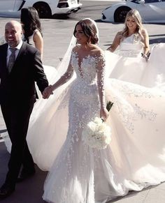 the bride and groom are holding hands as they walk down the street in their wedding gowns