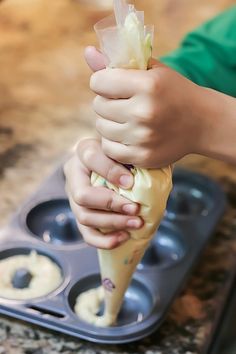 a person is holding an ice cream cone in front of a muffin pan with doughnut holes