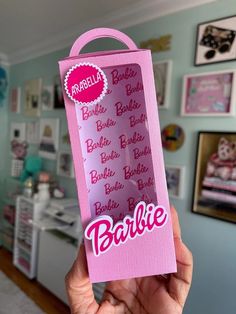 a person holding up a pink package with barbie's name written on the side