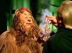 "Cowardly Lion Courage Medal Wizard of Oz 1939 movie The Cowardly Lion's badge of Courage is an ornate gold cross with \"COURAGE\" highlighted in blue and the crest in silver in the center. Add a red and white ribbon with a pin to secure it to clothing or the Lion's costume. In the Book Lions are supposed to be \"The Kings of Beasts,\" the Cowardly Lion believes that his fear makes him inadequate. He does not understand that courage means acting in the face of fear, which he does frequently. Onl Cowardly Lion Costume, Wizard Of Oz Lion, Lion Costume, Cowardly Lion, Glinda The Good Witch