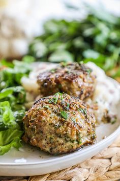 two meatballs on a plate with greens and mashed potatoes in the foreground