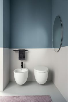 two white toilets sitting next to each other in a room with blue walls and a mirror on the wall