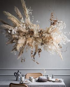 an arrangement of dried flowers hangs from the ceiling over a table with two cups and saucers on it