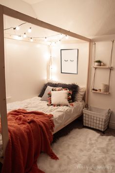 a bedroom with white walls and lights strung from the ceiling, bed frame is made up