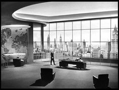 a man is walking in an office with large windows looking out on the city skyline