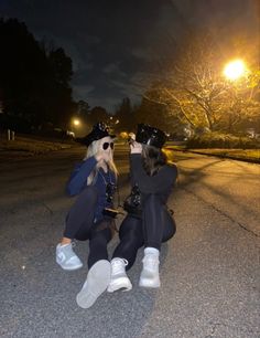 two women sitting on the ground at night taking pictures with their cell phones in front of them