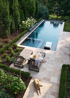 a woman laying on top of a chair next to a pool in a backyard with a dog