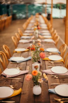 a long wooden table with plates and flowers in vases on each place setting for an event