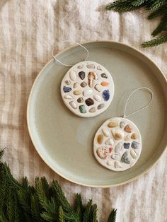 two ceramic ornaments are sitting on a plate next to some fir branches and pine needles