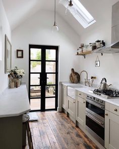 a kitchen with white walls and wooden floors has an open skylight above the stove