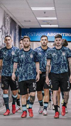 a group of men in soccer uniforms walking down a hallway with their feet on the ground