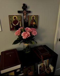 pink roses in a vase on top of a table next to an open book and crucifix