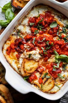 a white casserole dish filled with tomato sauce and cheese, garnished with fresh basil