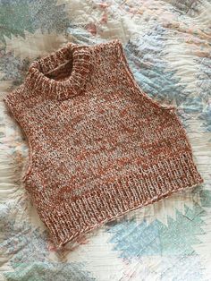 an orange sweater sitting on top of a bed next to a white and blue blanket