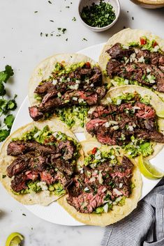 four steak tacos on a plate with limes and cilantro